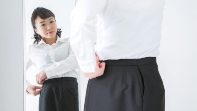 姿見の前で服のサイズを気にする女性