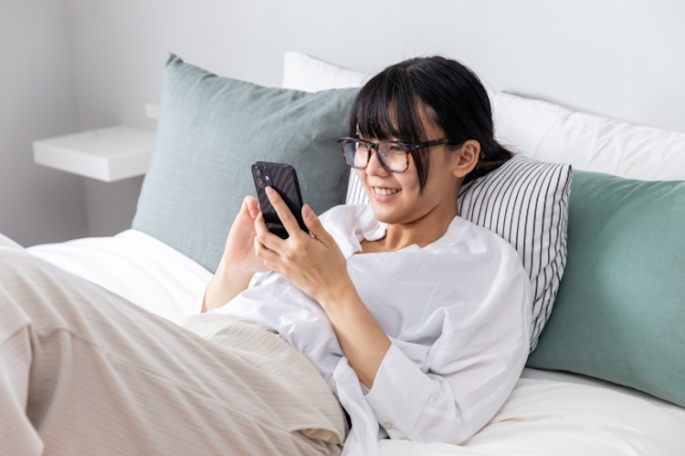 ベットでスマホを操作する女性
