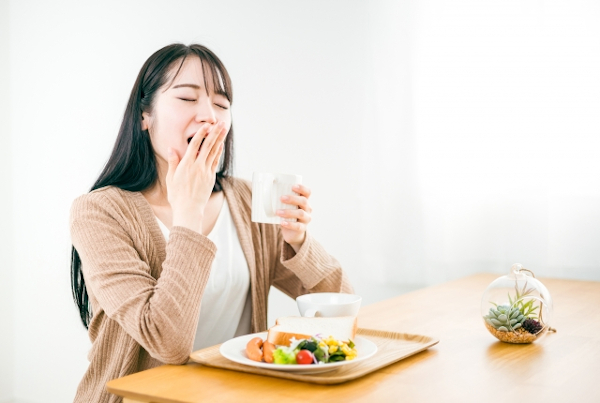 あくびをしながら朝食を食べる女性